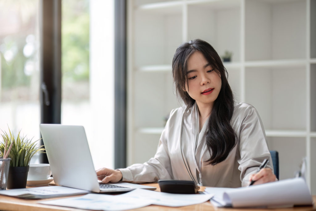 Asian Business Woman Using Laptop For Doing Math Finance On An Office Desk, Tax, Report, Accounting, Statistics, And Analytical Research Concept - Planconta Contabilidade